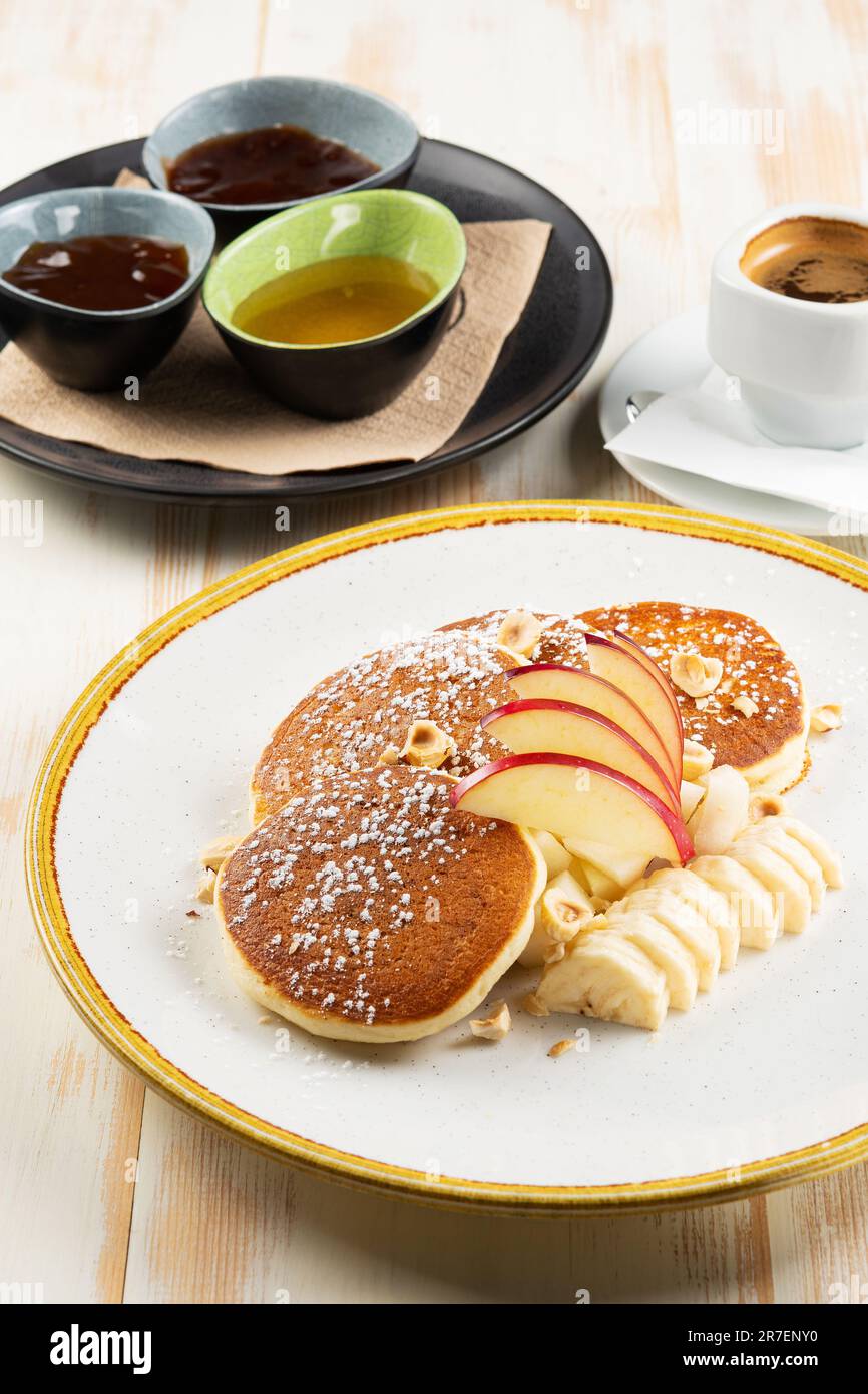 Frittelle con frutta e tazza di caffè su sfondo di legno bianco. Colazione gustosa. Foto Stock