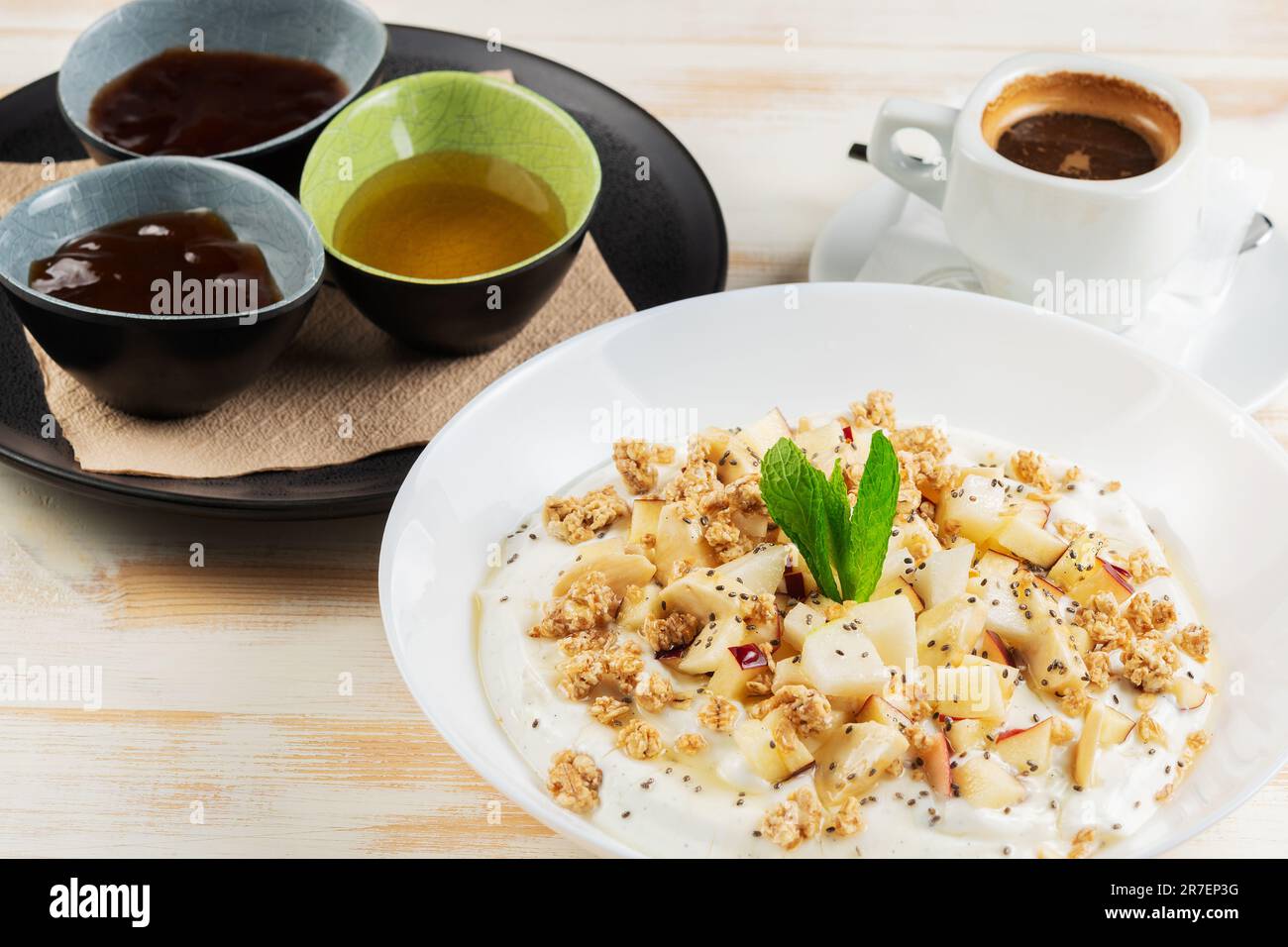 Yogurt con fiocchi, frutta e tazza di caffè su sfondo di legno bianco. Βreakfast concetto. Foto Stock