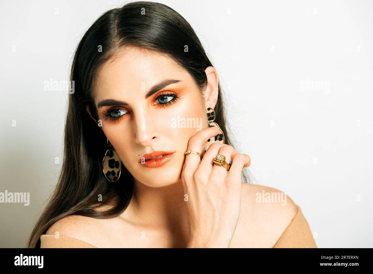 Studio shot di bella giovane donna con capelli scuri e occhi blu, con vestito marrone a spalla aperta Foto Stock