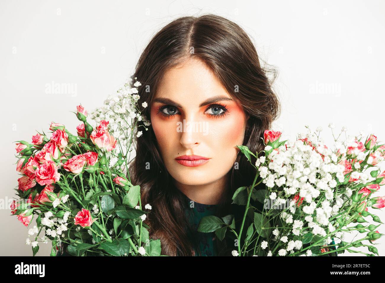 Studio shot di bella donna con lunghi capelli scuri, trucco rosa brillante, vestito verde, tenendo bouquet di rose piccole Foto Stock