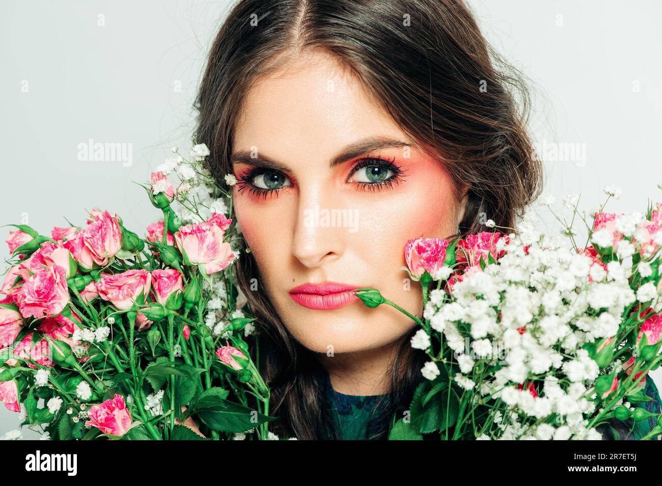 Studio shot di bella donna con lunghi capelli scuri, trucco rosa brillante, vestito verde, tenendo bouquet di rose piccole Foto Stock