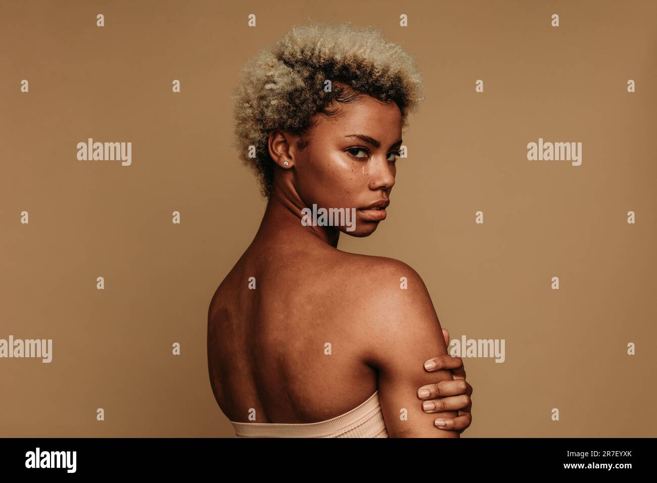 Giovane donna nera si alza in uno studio, guardando direttamente nella fotocamera con un'espressione emotiva. La sua faccia macchiata a strappo incarna la lotta di fe Foto Stock