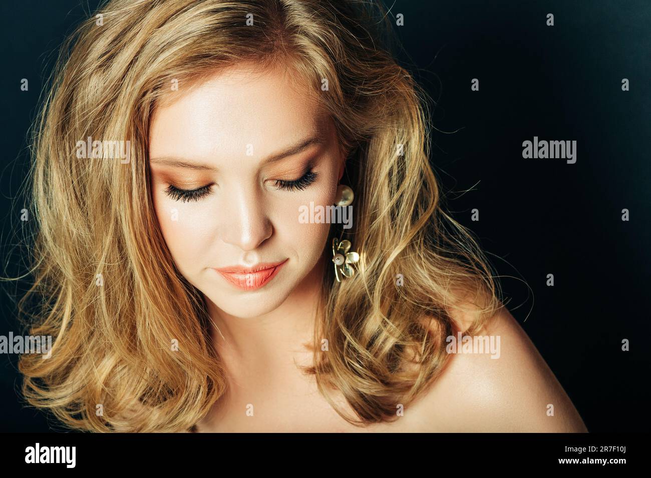 Primo piano ritratto di bella giovane donna con capelli biondi e make up professionale, posa su sfondo nero, guardando verso il basso Foto Stock