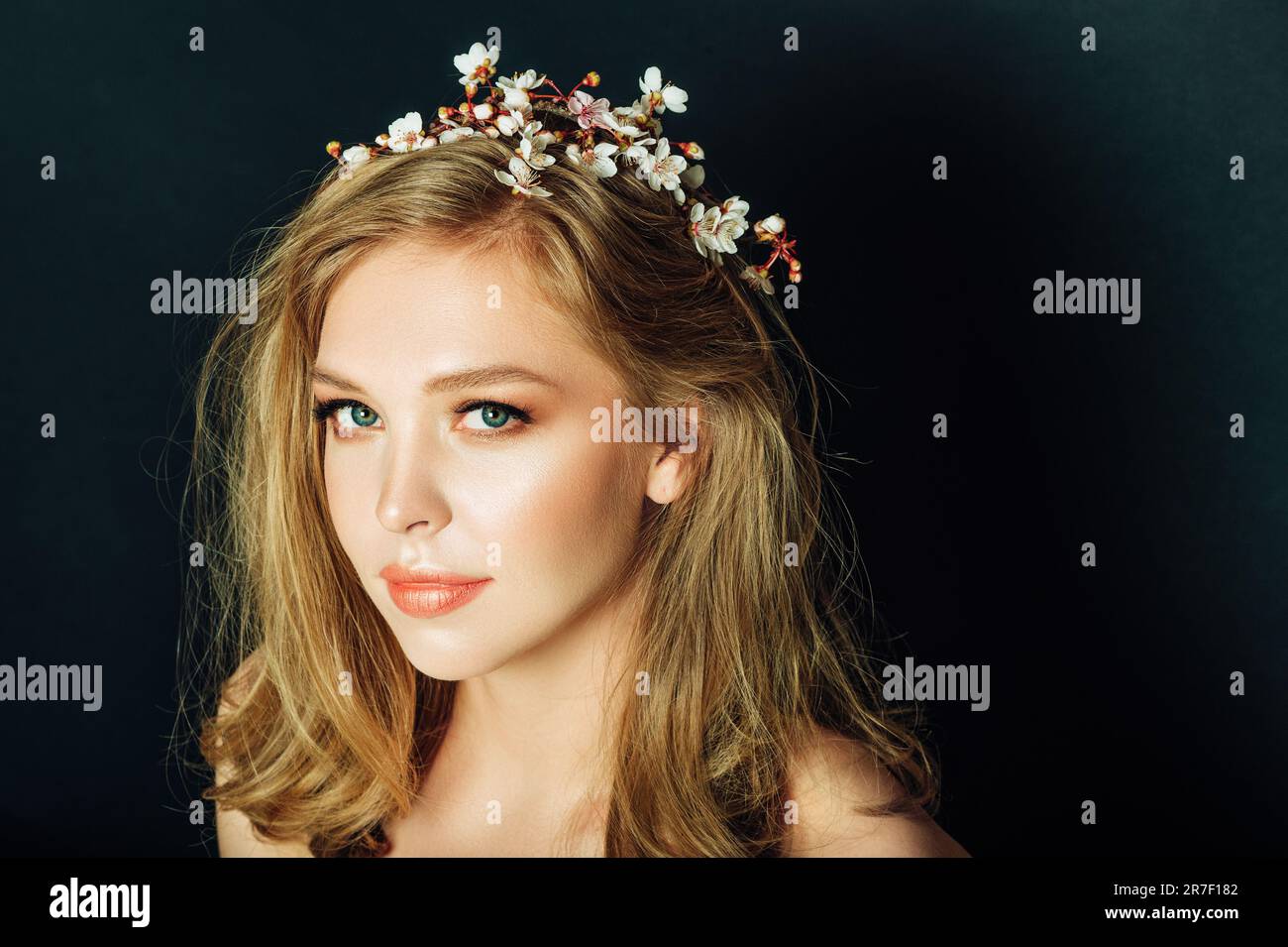 Primo piano ritratto di bella giovane donna con capelli biondi e make up professionale, posa su sfondo nero, indossando primavera fioritura ramo di pisello Foto Stock