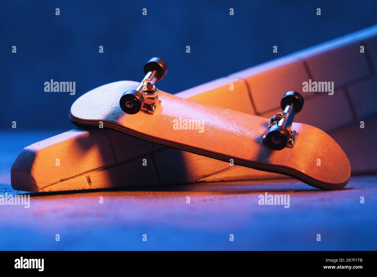 Una piccola skateboard o fingerboard illuminata da luci colorate su una rampa di intonaco. Foto Stock