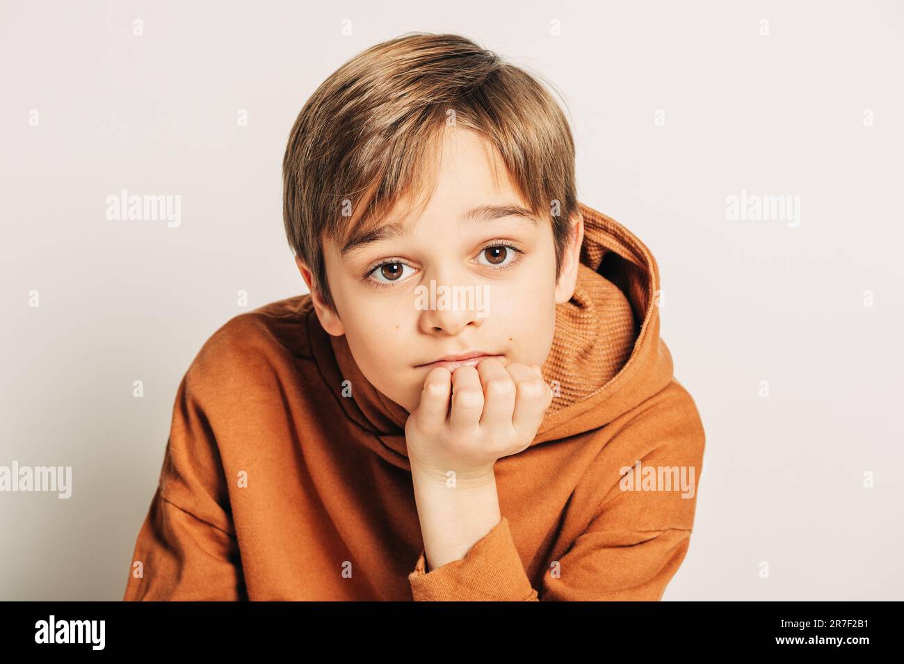 Studio di un bel ragazzo di 10 anni con capelli biondi, con cappuccio marrone, posato su sfondo bianco Foto Stock