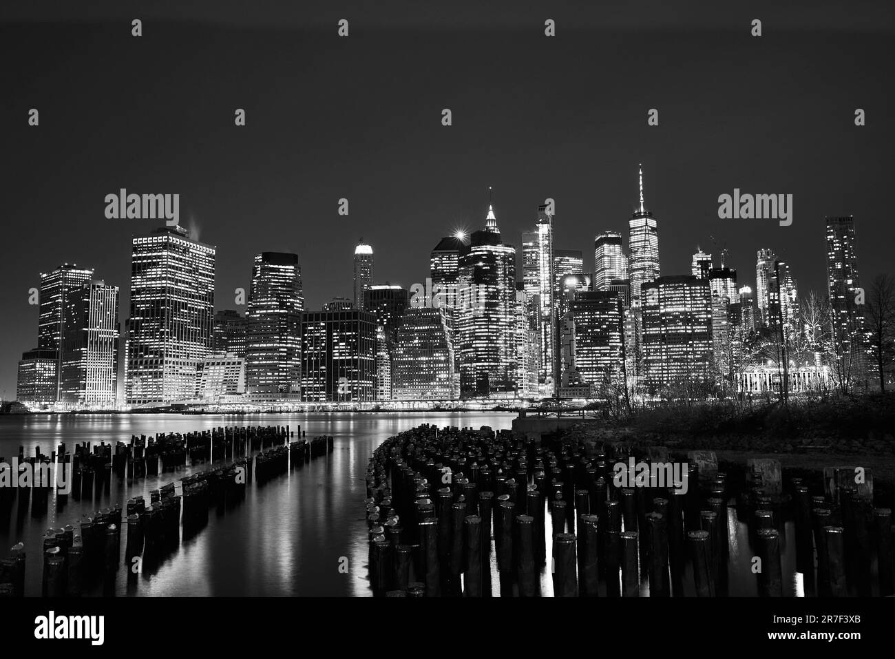 Un'immagine in scala di grigi dello skyline di New York City con una linea di pali in legno in primo piano. Foto Stock