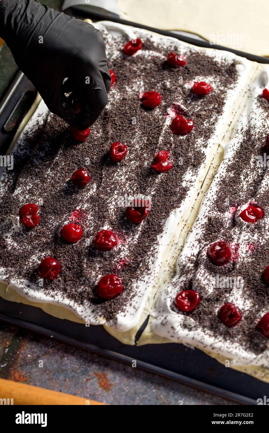 Processo di preparazione di una torta Napoleone con semi di papavero e ciliegie. Primo piano Foto Stock