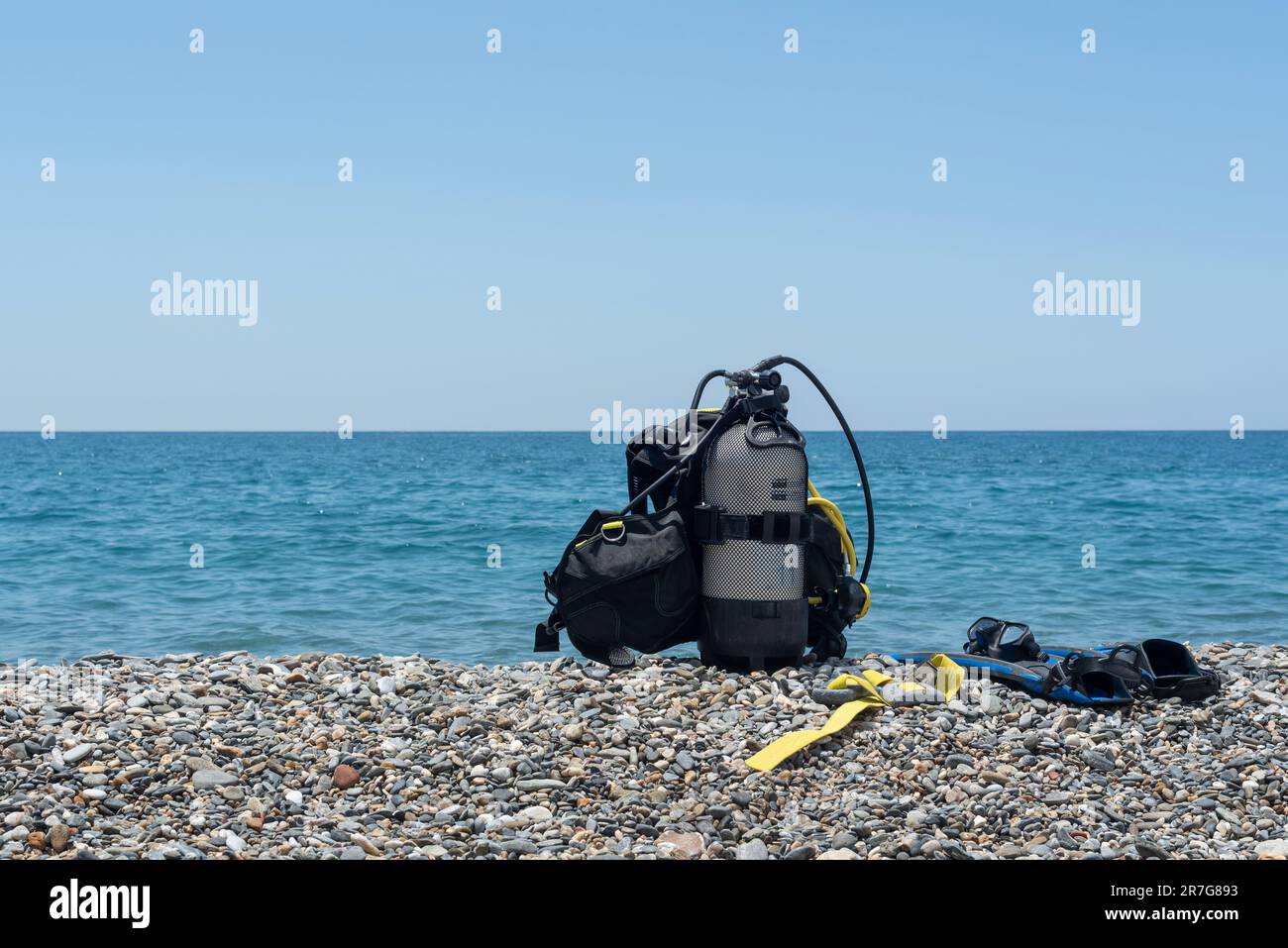 Attrezzatura subacquea, tra cui serbatoio di ossigeno, pinne, occhiali, regolatore e pesi sulla riva di una spiaggia rocciosa. Sport acquatici. Iniziazione all'immersione subacquea Foto Stock