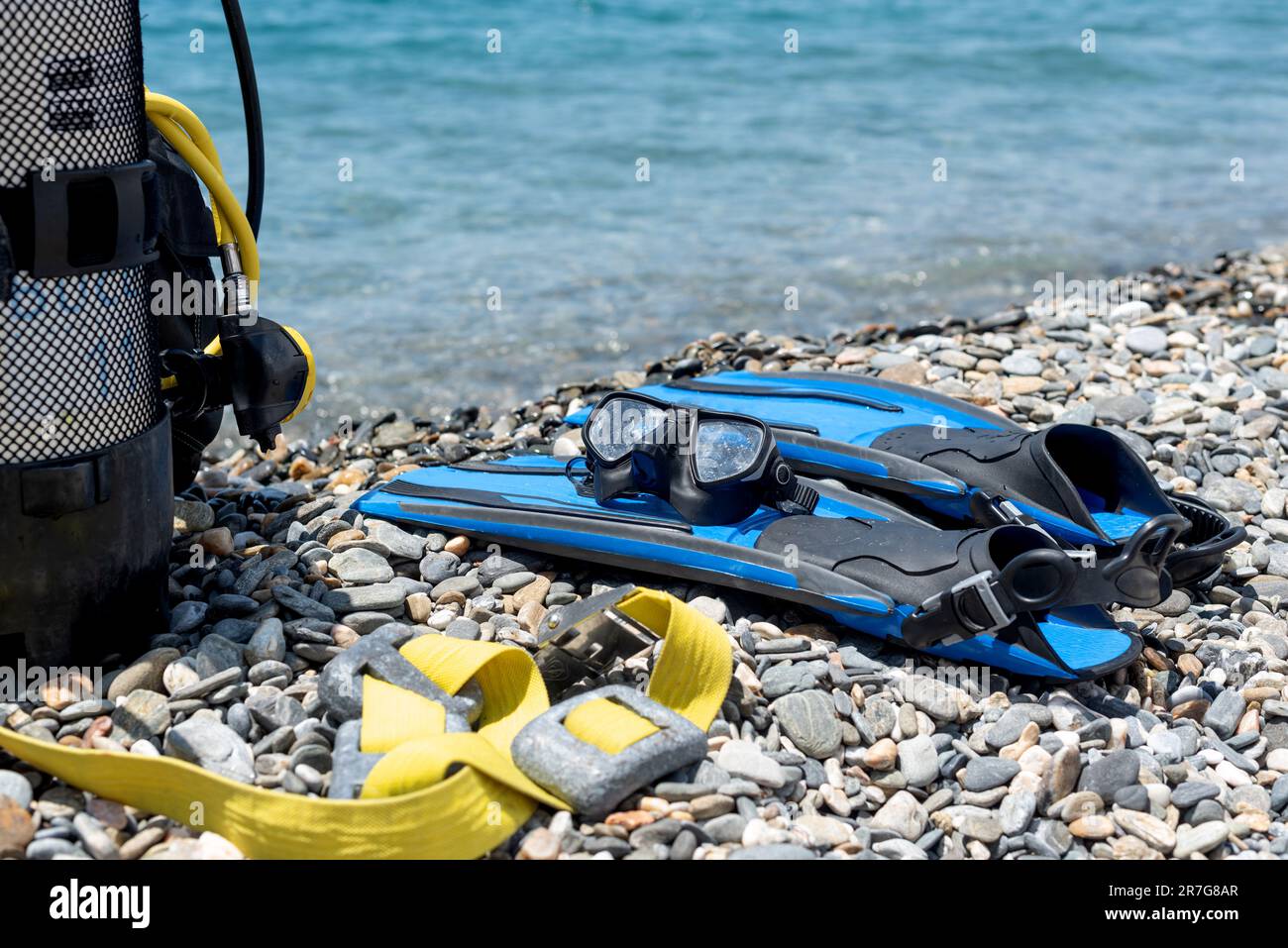 Attrezzatura subacquea, tra cui serbatoio di ossigeno, pinne, occhiali, regolatore e pesi sulla riva di una spiaggia rocciosa. Sport acquatici. Iniziazione all'immersione subacquea Foto Stock