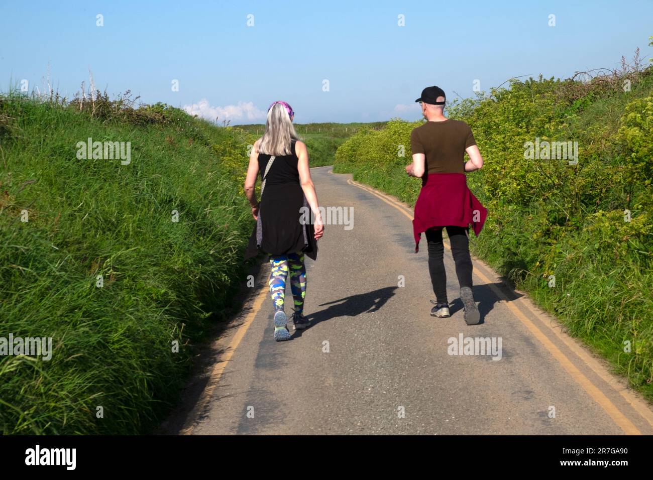 Vista posteriore della coppia di due amici che camminano lungo una strada di campagna in estate nella soleggiata giornata primaverile del 2023 maggio Pembrokeshire Galles UK KATHY DEWITT Foto Stock