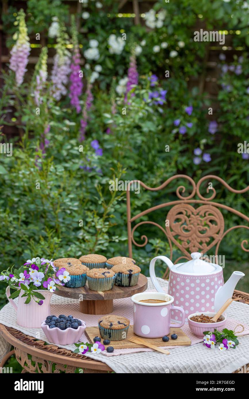decorazione da tavolo con muffin ai mirtilli, tazza di caffè e bouquet di fiori di viola nel giardino estivo Foto Stock