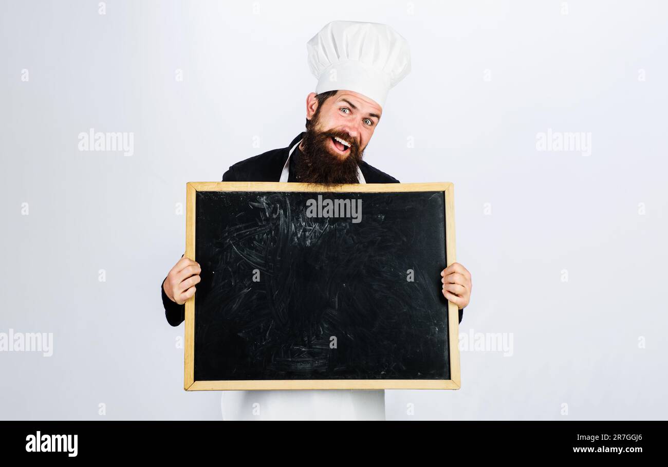 Sorridente chef maschio con lavagna vuota. Menu per pranzo di lavoro. Chef del ristorante che mostra cartellone vuoto con spazio per la copia del testo. Chef maschile, cuoco o. Foto Stock