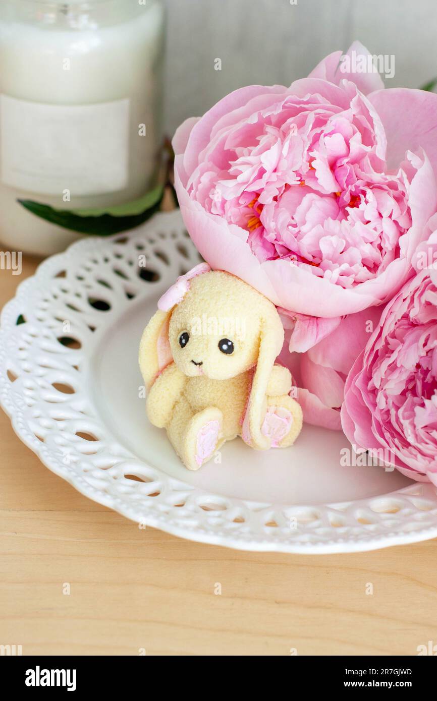 Carino coniglietto commestibile fatto di cioccolato bianco con fiori di peonia e candele Foto Stock