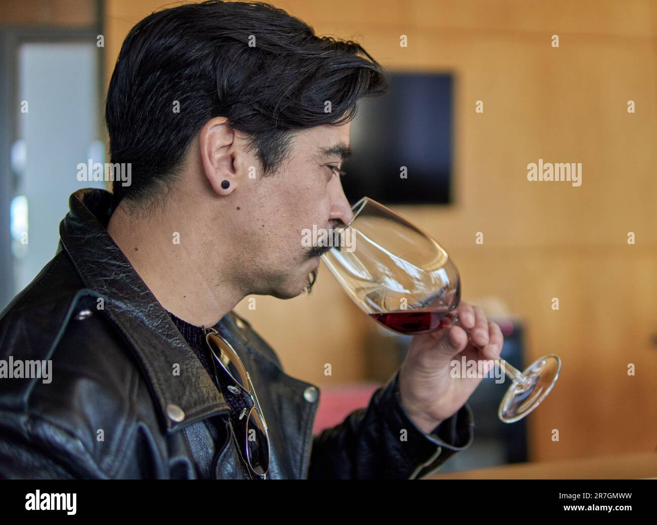 uomo latino in profilo ad una degustazione di vini in una cantina a mendoza argentina. Uomo brunetta in giacca di pelle con baffi che trattengono e odorano seriamente Foto Stock