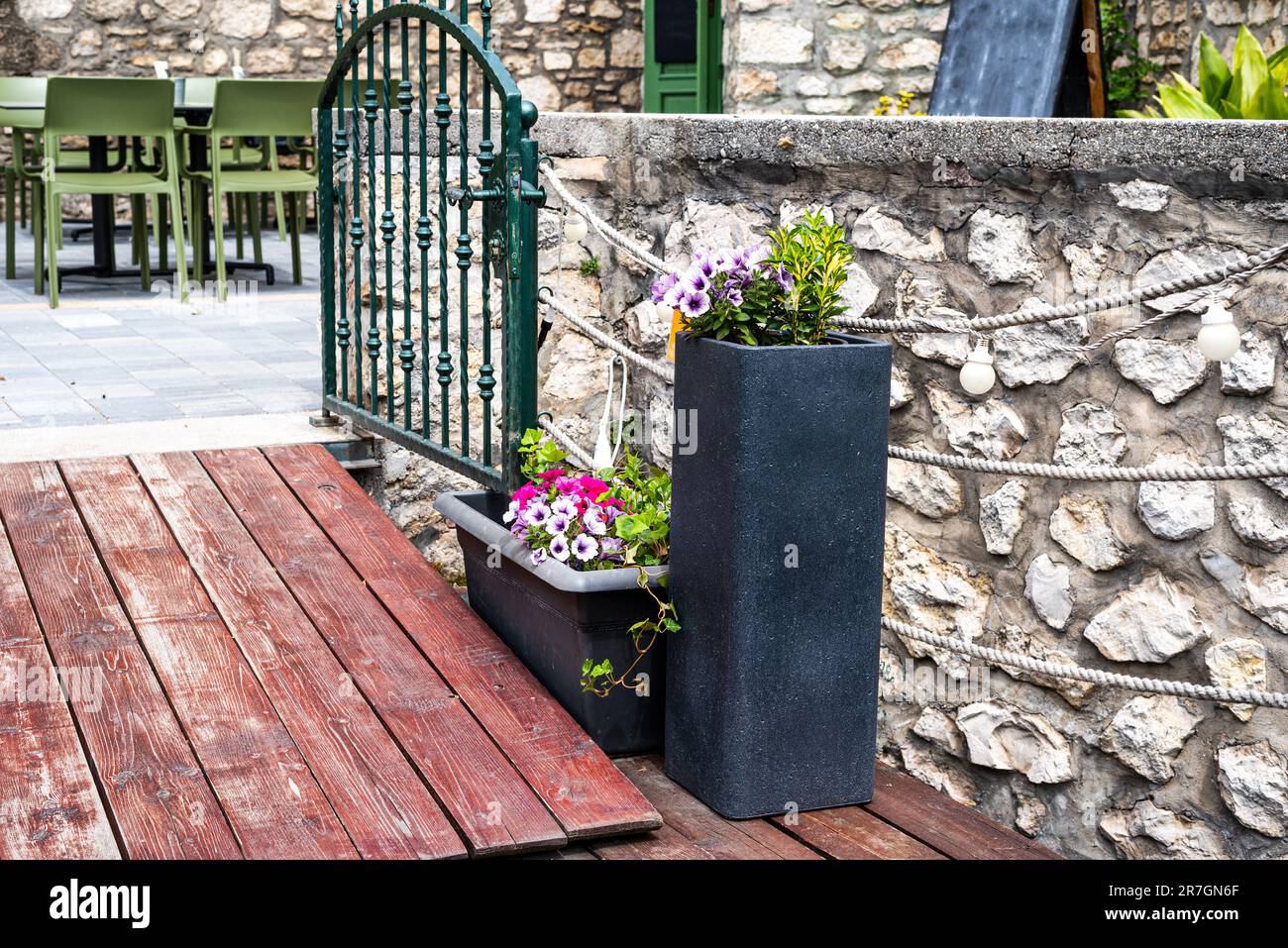Un'entrata decorata con fiori con cancello metallico verde ad un bar o ristorante con un'atmosfera mediterranea. Foto Stock