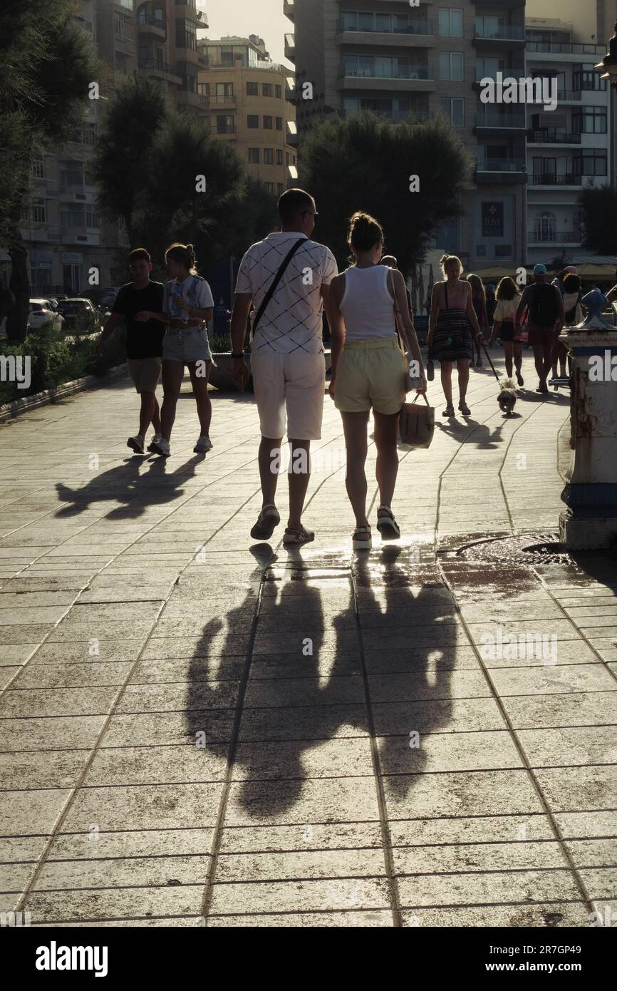 Due coppie a piedi luce del sole dietro sul lungomare di Sliema, Malta Foto Stock