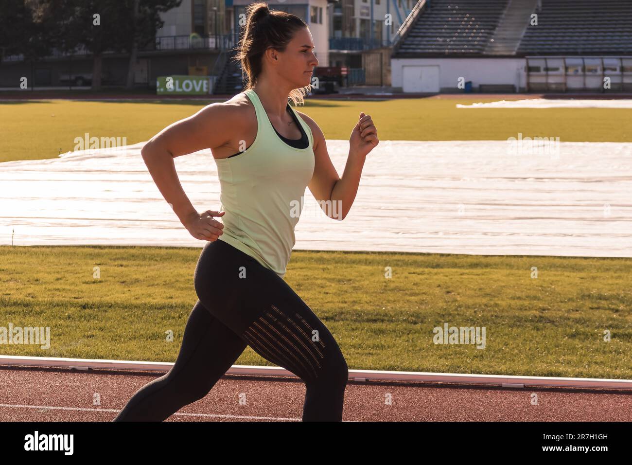Giovane atleta caucasica, forte e muscolosa, in esecuzione su una pista atletica all'aperto, tiro medio. Foto Stock