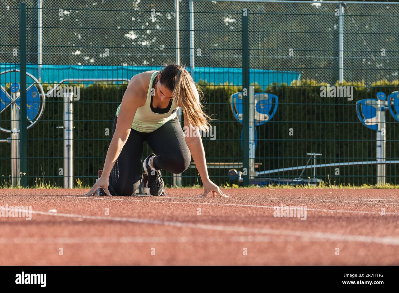 Giovane donna che si prepara alla corsa, prendendo una posizione di partenza per lo sprint, utilizzando il blocco di partenza Foto Stock