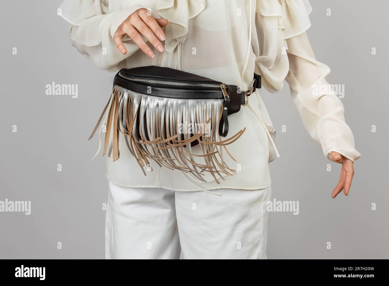 Donna bianca che indossa abiti bianchi e tracolla Borsa da cintura in pelle nera con frangia argentata decorativa su sfondo grigio Foto Stock
