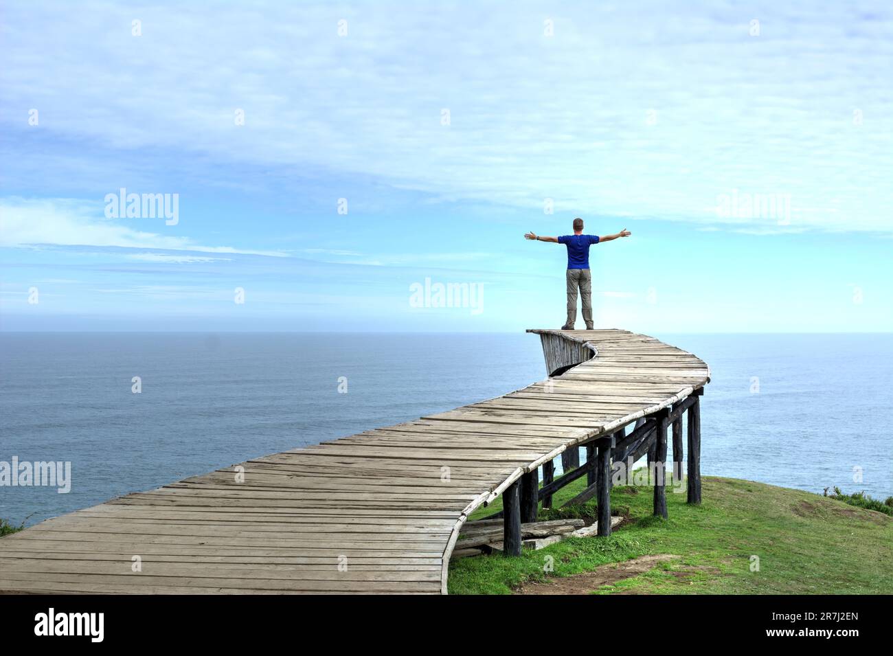 Un uomo si trova sul bordo di una lunga passerella in legno (il "Dock of Souls" di Chiloé) e guarda l'oceano all'orizzonte in una giornata limpida Foto Stock