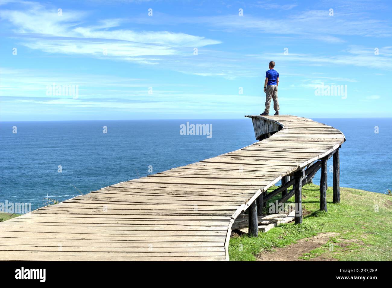 Un uomo si trova sul bordo di una lunga passerella in legno (il "Dock of Souls" di Chiloé) e guarda l'oceano all'orizzonte in una giornata limpida Foto Stock