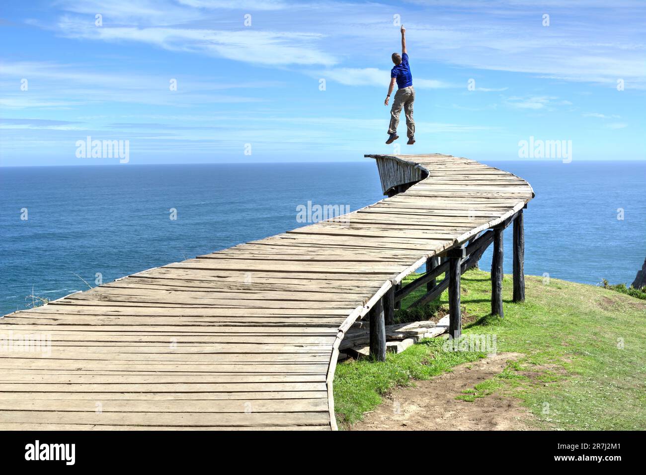 Un uomo si trova sul bordo di una lunga passerella in legno (il "Dock of Souls" di Chiloé) e guarda l'oceano all'orizzonte in una giornata limpida Foto Stock