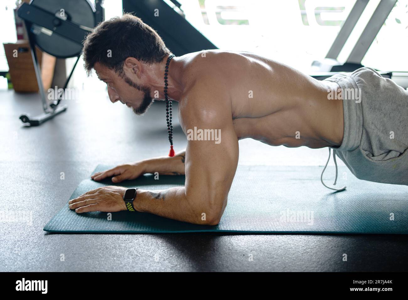 L'uomo che fa le esercitazioni di nucleo mentre fa l'asse su un tappetino in una palestra Foto Stock