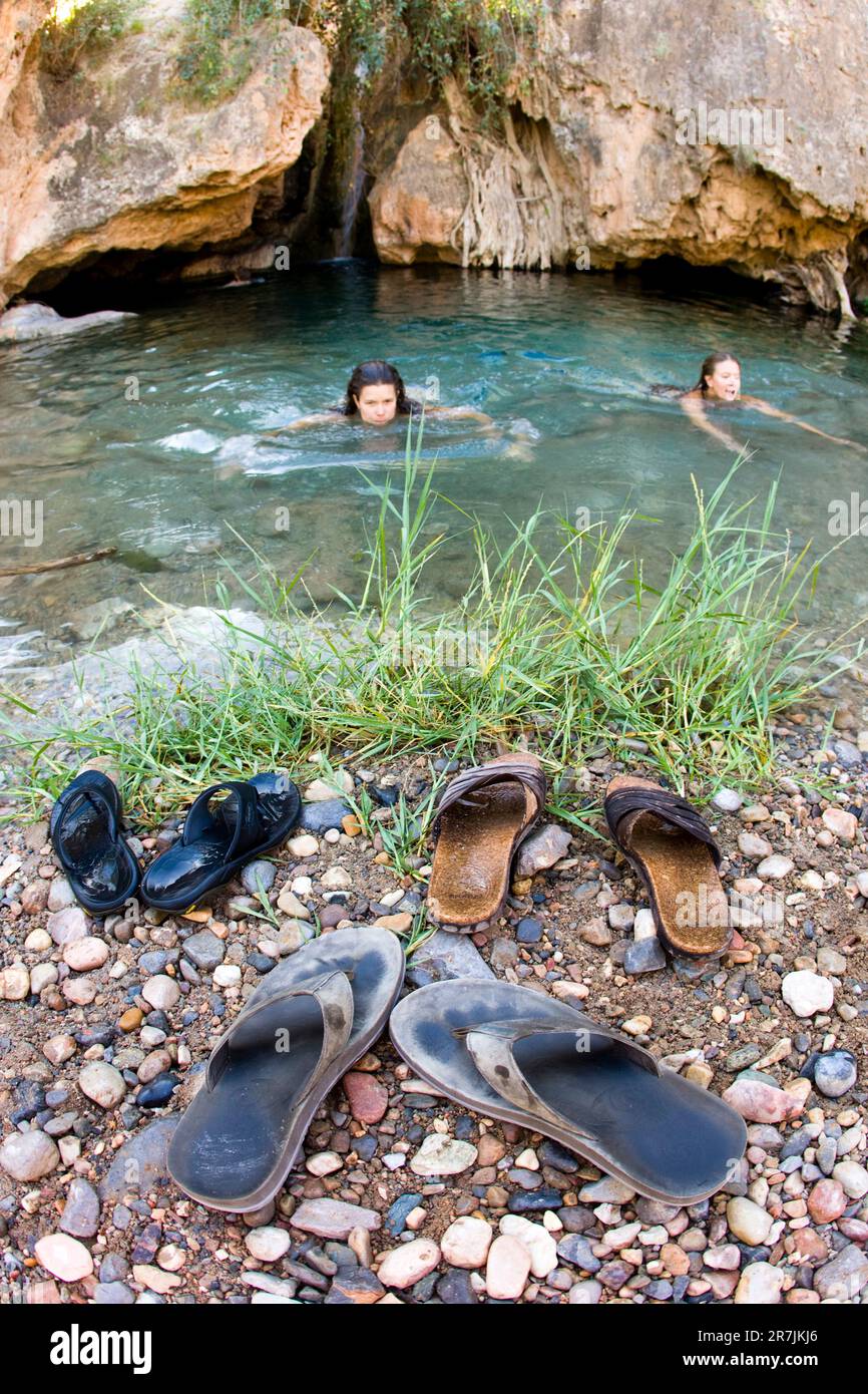 Due femmine che si godono un tuffo rinfrescante in una buca per nuotare. Infradito che siede sul bordo del foro. Acqua cristallina. Foto Stock
