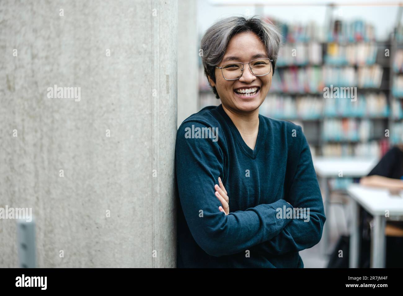 Ritratto di sorridente studente asiatico in piedi con le braccia incrociate in biblioteca del college Foto Stock