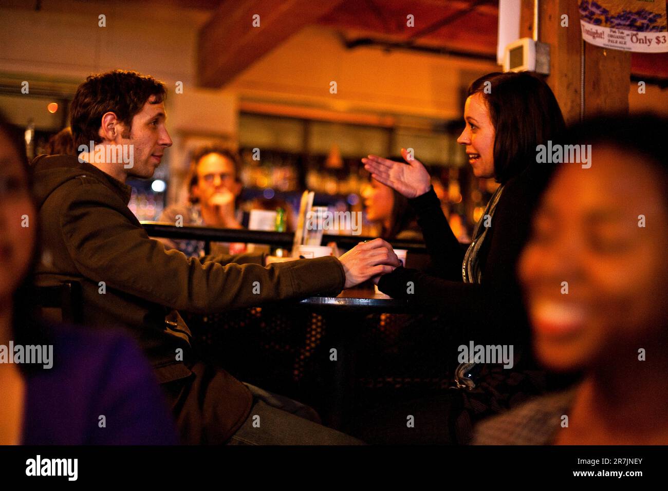 Un giovane uomo alla moda tiene la mano di una donna durante una conversazione in un bar a Seattle, Washington. Foto Stock