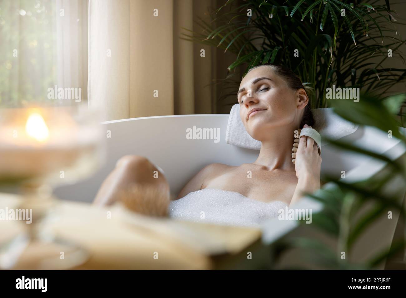 donna che gode di vasca idromassaggio con schiuma e spazzola per massaggio corpo Foto Stock