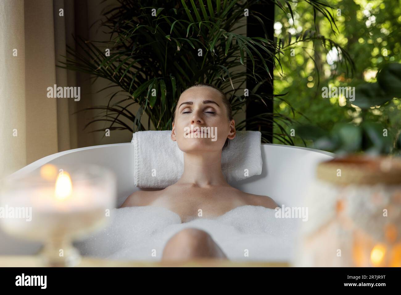 donna che gode di vasca idromassaggio con schiuma e candele profumate. cura del corpo, aromaterapia e benessere mentale Foto Stock