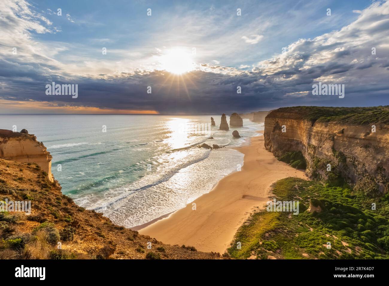Australia, Victoria, Vista del sole che splende attraverso le nuvole di tempesta sulla spiaggia sabbiosa nel Parco Nazionale di Port Campbell con dodici Apostoli sullo sfondo Foto Stock