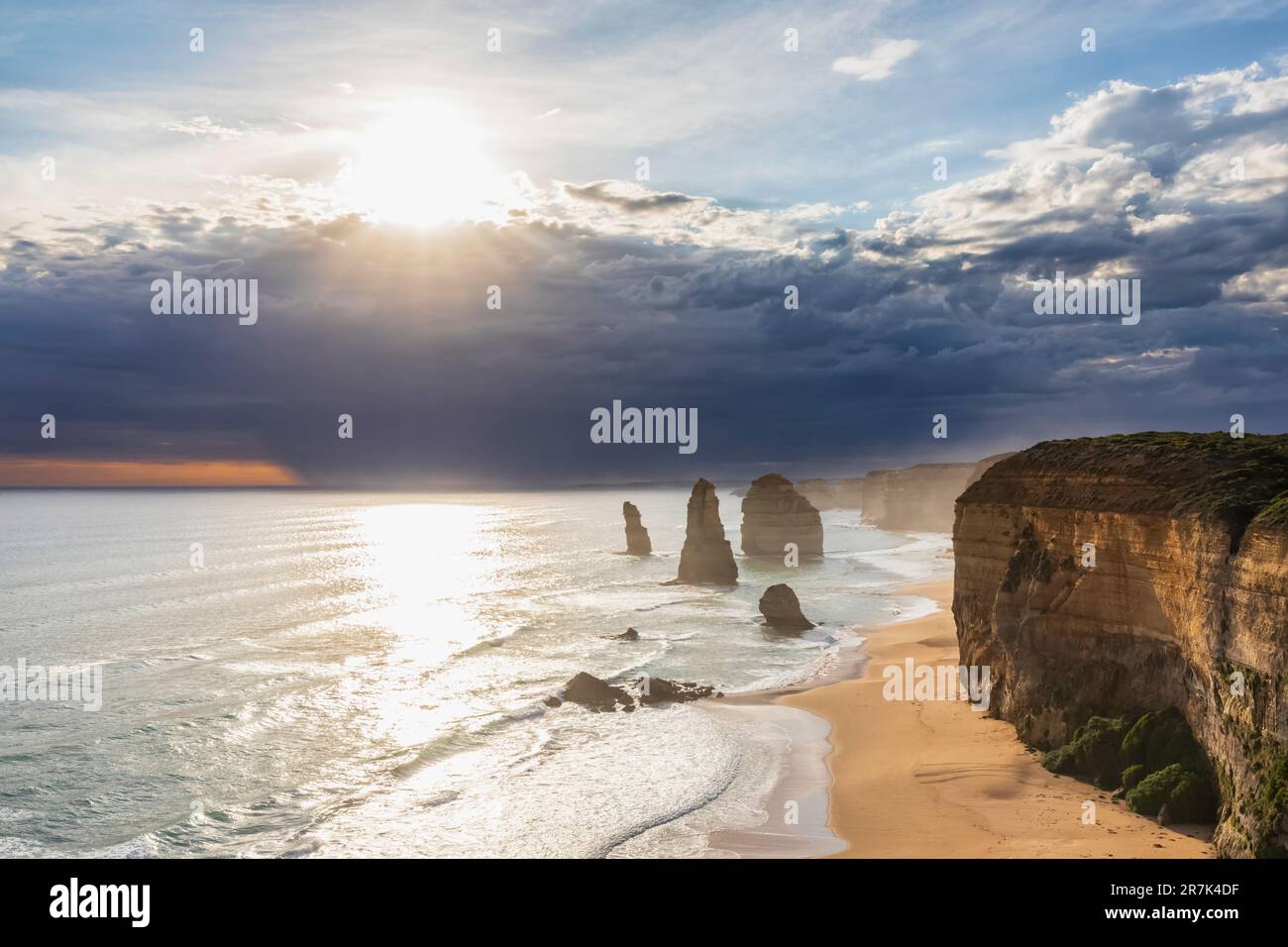 Australia, Victoria, Vista del sole che splende attraverso le nuvole di tempesta sulla spiaggia sabbiosa nel Parco Nazionale di Port Campbell con dodici Apostoli sullo sfondo Foto Stock