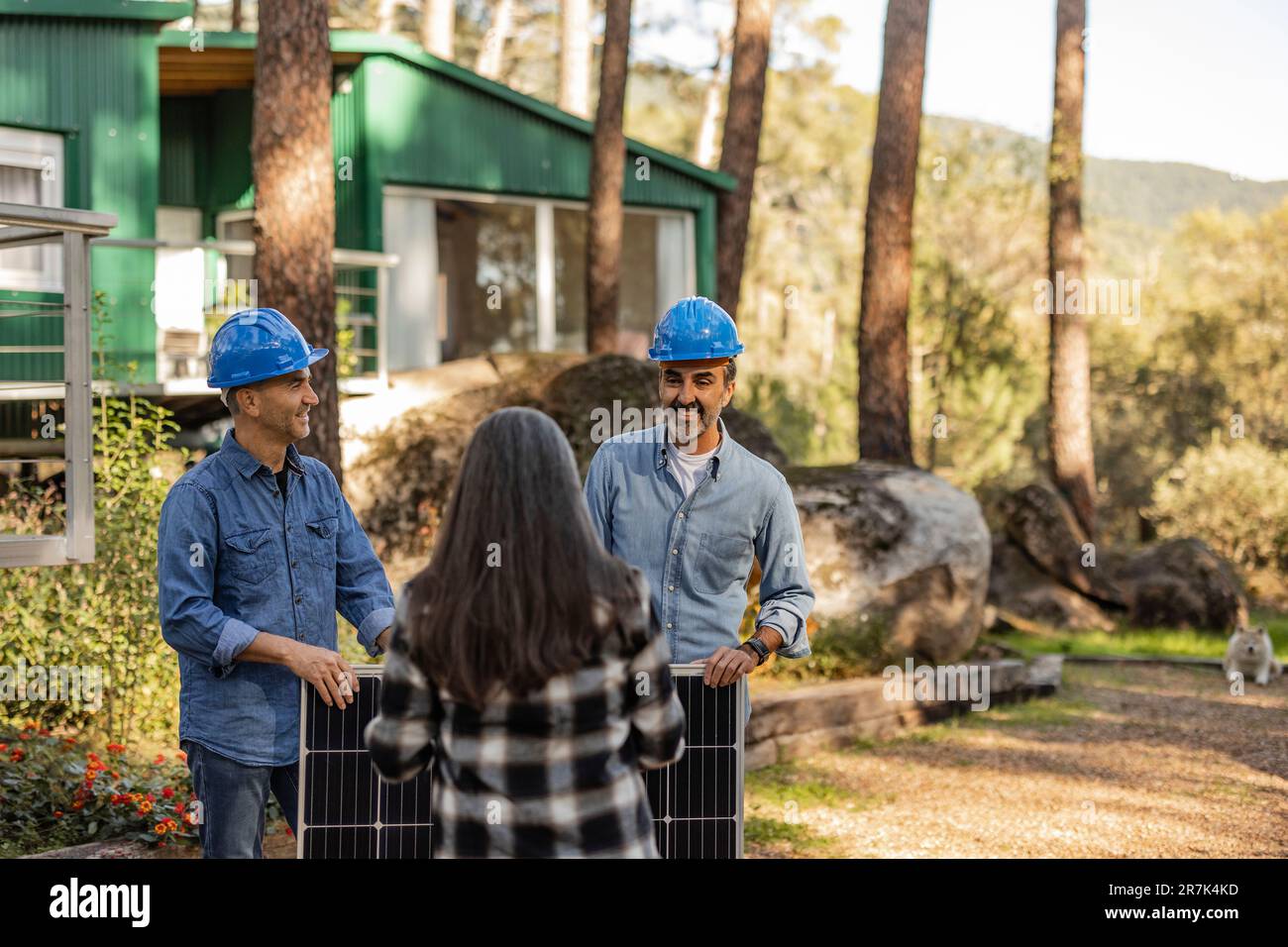 Il proprietario di casa che parla con i tecnici fotovoltaici che trasportano il pannello solare Foto Stock