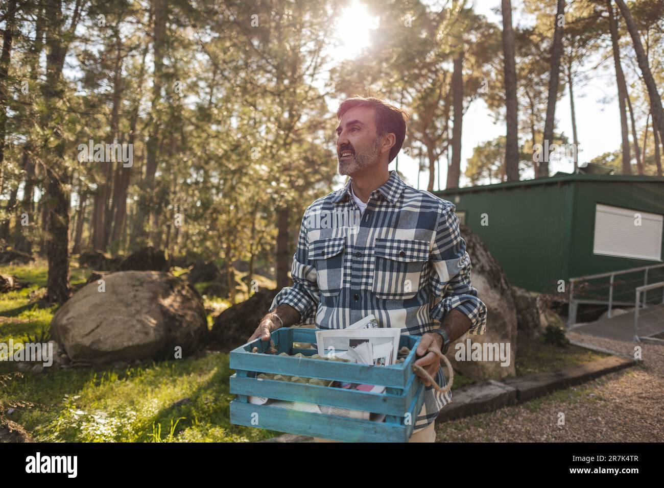 Uomo maturo che trasporta la cassa con i rifiuti separati in giardino Foto Stock