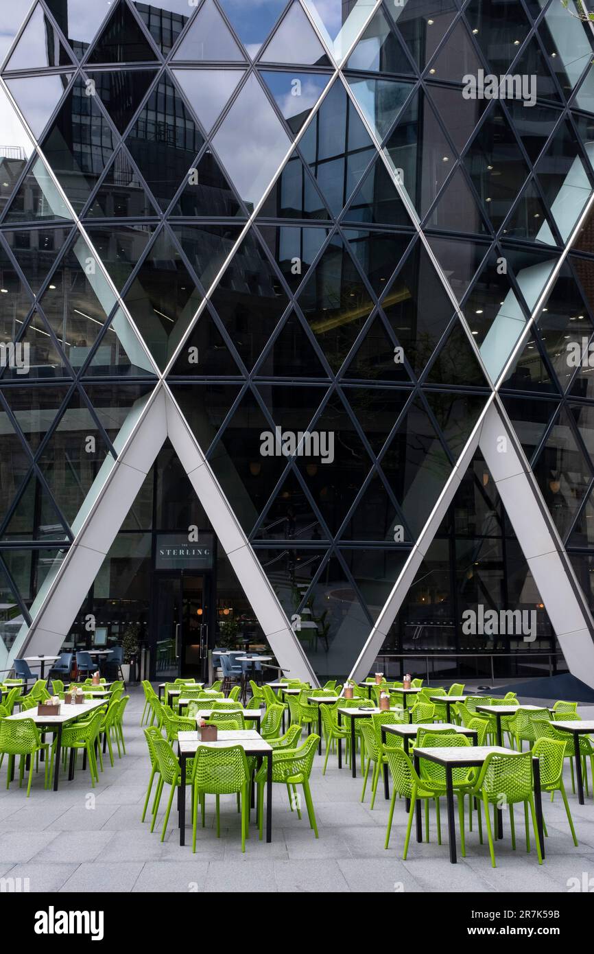 30 St Mark Axe, affettuosamente soprannominato il Gherkin contrasta con tavoli e sedie verdi nella City of London il 25th maggio 2023 a Londra, Regno Unito. La City of London è una città, una contea cerimoniale e un distretto governativo locale che contiene il principale distretto finanziario centrale CBD di Londra. La città di Londra è ampiamente indicata semplicemente come la città è conosciuta anche colloquialmente come il miglio quadrato. Foto Stock