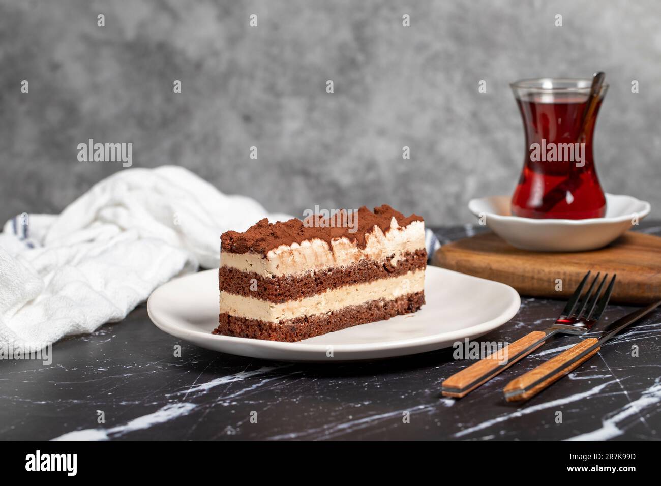 Dolce tradizionale italiano tiramisù torta. Fetta di torta al cioccolato con crema di tiramisù e polvere di cacao sul tavolo scuro. Foto Stock