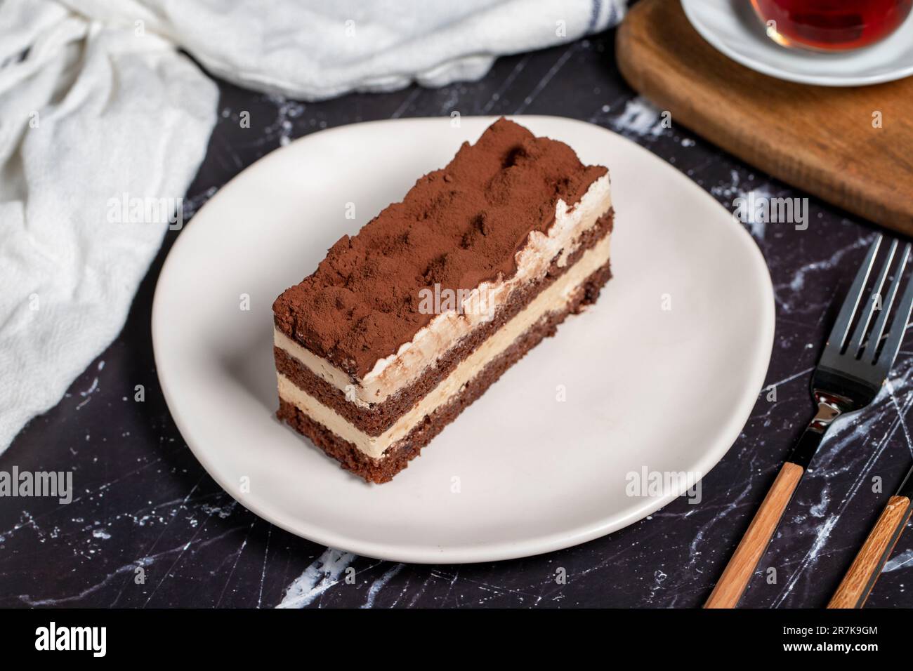 Dolce tradizionale italiano tiramisù torta. Fetta di torta al cioccolato con crema di tiramisù e polvere di cacao sul tavolo scuro. Foto Stock