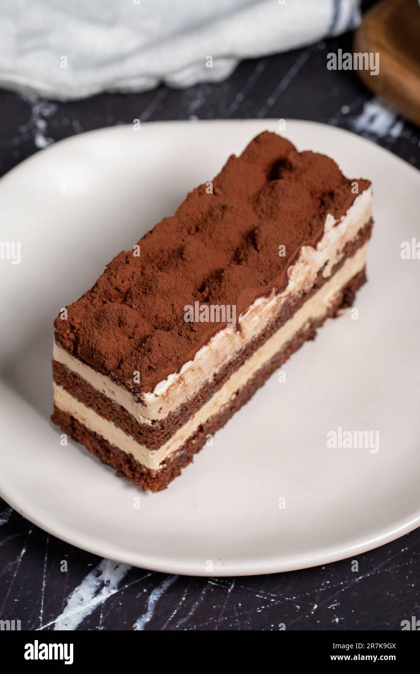 Dolce tradizionale italiano tiramisù torta. Fetta di torta al cioccolato con crema di tiramisù e polvere di cacao sul tavolo scuro. Foto Stock