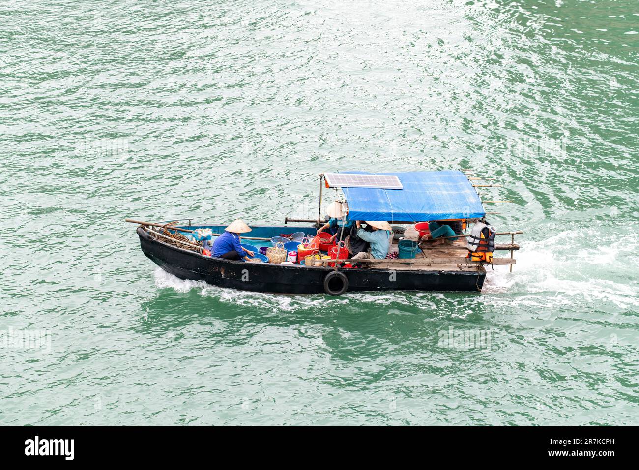 Vista ravvicinata ad alto angolo di una piccola barca da pesca in legno nelle acque della Baia di ha Long, Vietnam con una donna con cappello di paglia che si prende cura della cattura del giorno Foto Stock