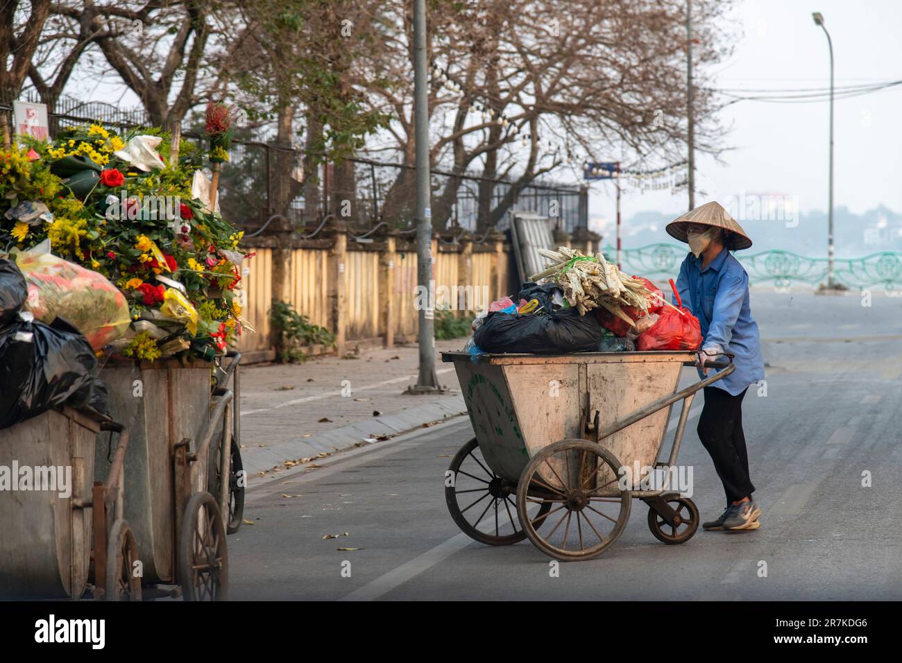Hanoi, Vietnam-aprile 2023; primo piano di una donna vietnamita che spinge un carrello spazzatura in strada sormontato da rifiuti tra cui fiori Foto Stock