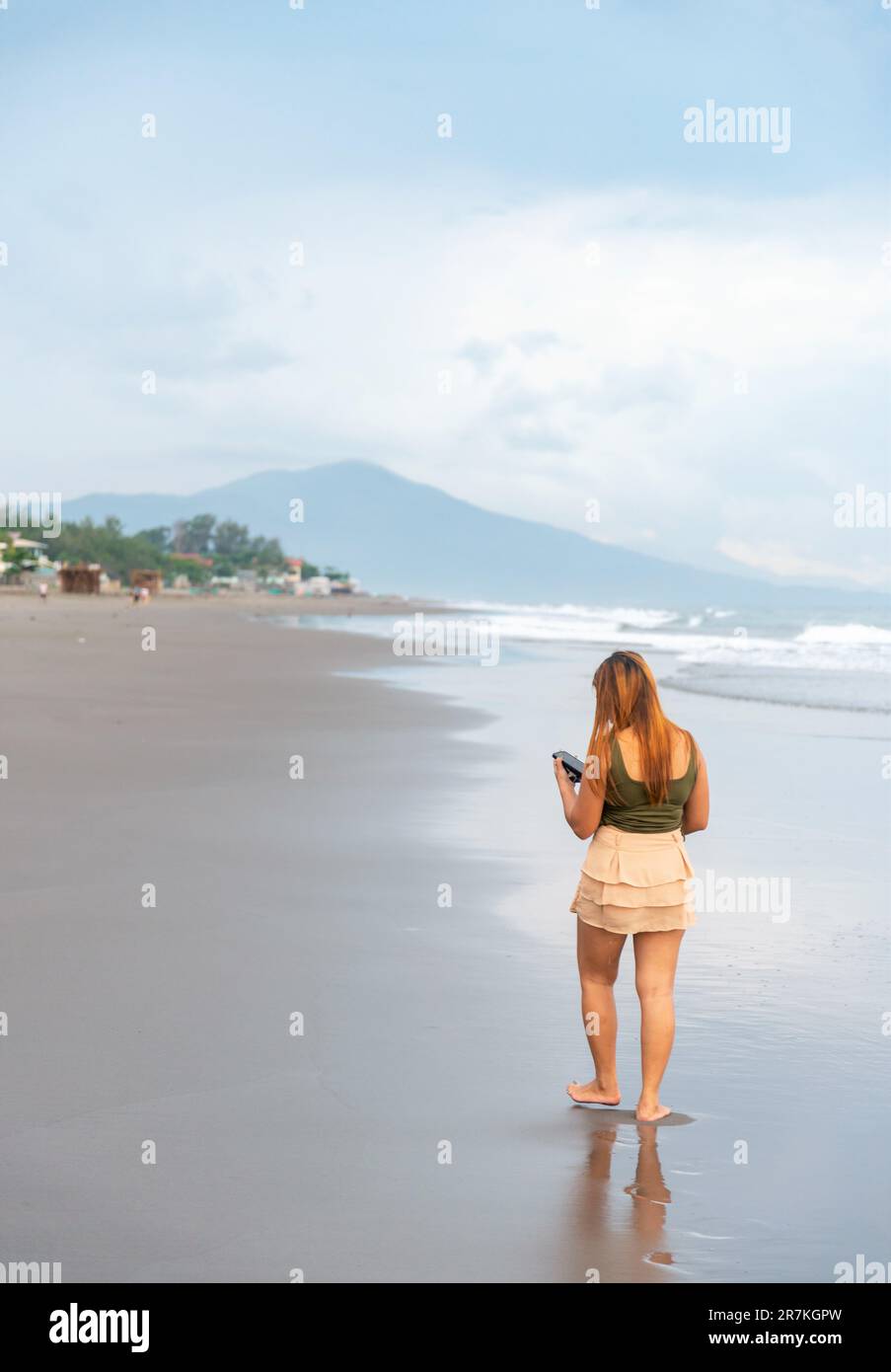 Tenendo il suo telefono per selfie, su una spiaggia vicino Manila al tramonto, aimlessly passeggiando le calde acque costiere, lungo le sabbie lisce, avendo divertimento, ballando aroun Foto Stock