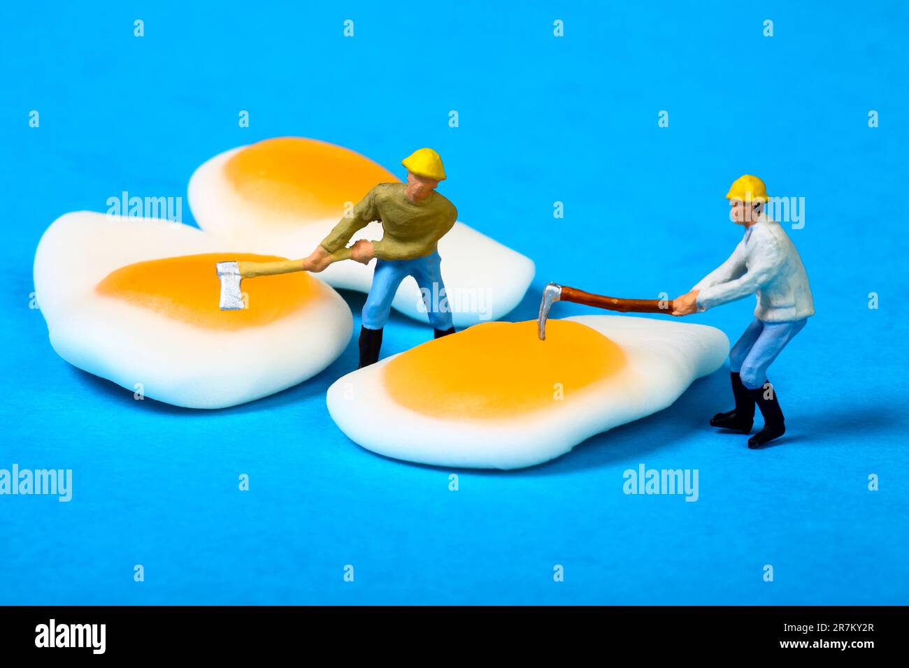 Immagine concettuale di figure in miniatura persone che cercano di far scoppiare i tuorli di caramelle all'uovo fritte Foto Stock
