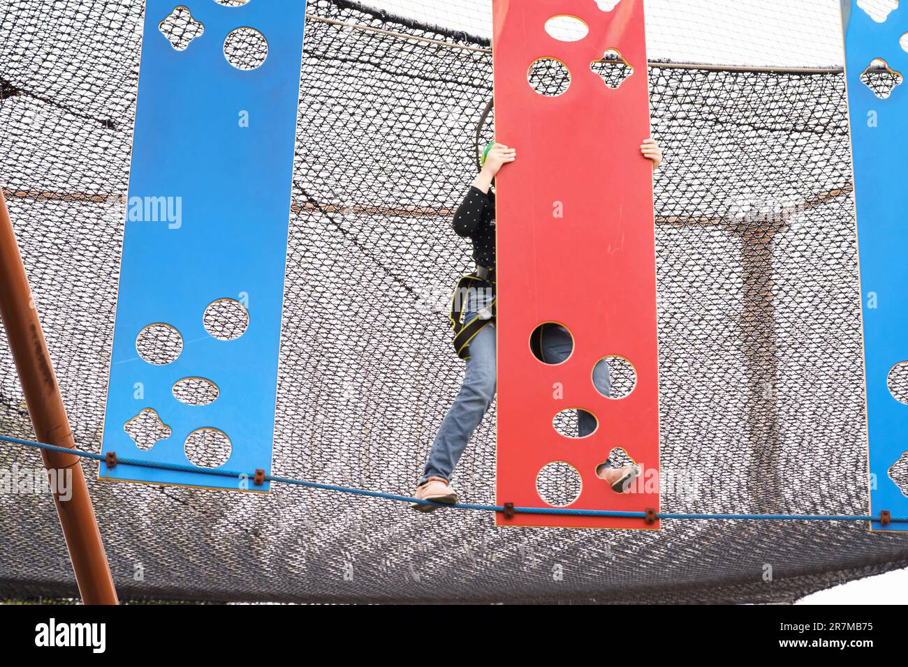 Adolescente ragazza in attrezzatura di arrampicata imbracatura, casco verde sport di sicurezza. Parco divertimenti Rope. Fissaggio del moschettone alla fune di sicurezza. Hangin Foto Stock