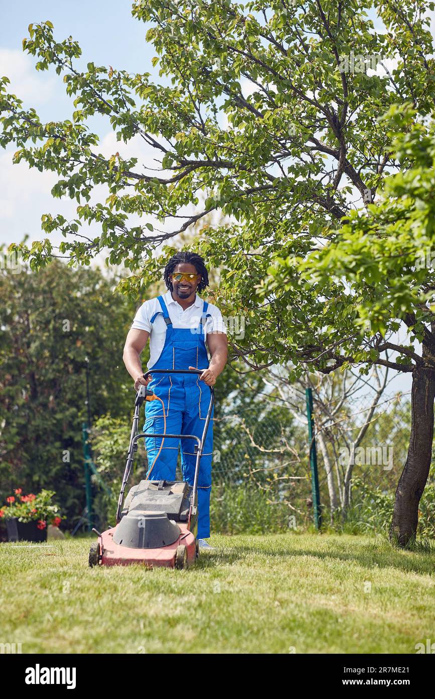 L'uomo afro-americano gestisce con sicurezza un rasaerba.con un'espressione mirata e una presa salda sulle impugnature, fa scorrere senza sforzo il rasaerba su t Foto Stock
