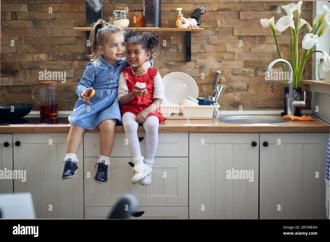 Due ragazze, una con la pelle giusta e l'altra con una carnagione scura radiante, ripartendo il abbraccio e le delizie squisite nella cucina. Foto Stock