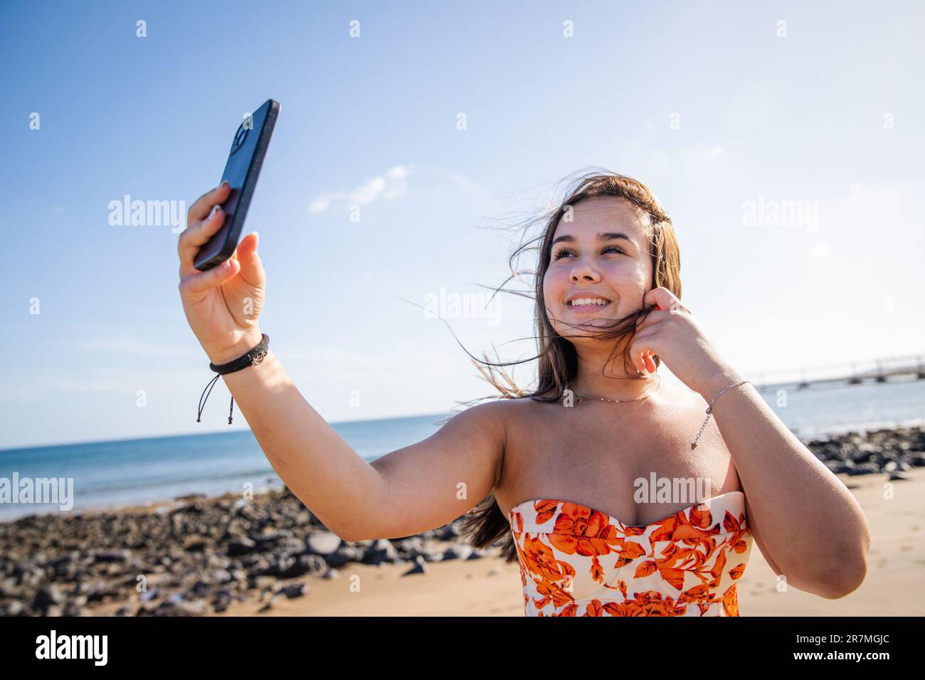 Una ragazza adolescente prende un selfie alla spiaggia in una giornata ventosa Foto Stock