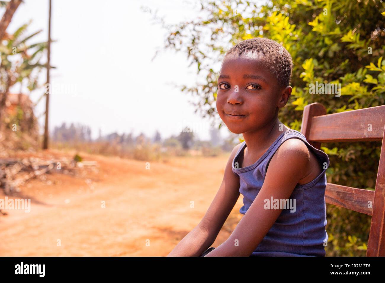 Ritratto di un ragazzino africano sorridente seduto su una sedia, sguardo innocente, foto con spazio copia Foto Stock